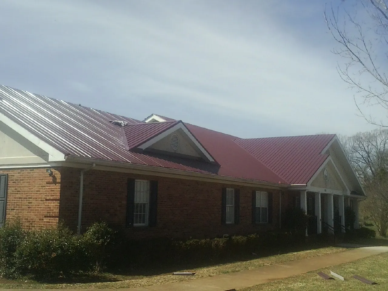Red metal roof with gabled entries on a long brick building, from a Hail Damage Roof Repair job in Saint Stephen