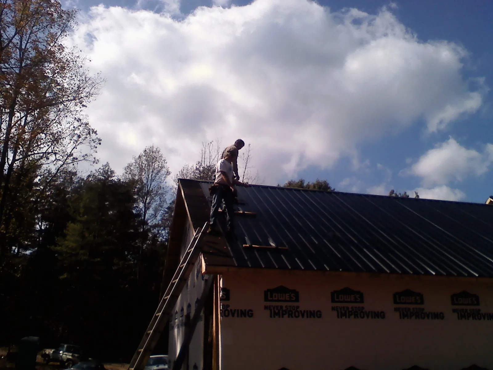 Roofer fastening dark metal panels high against a cloudy sky, from a Roof Inspection job in Saint Stephen