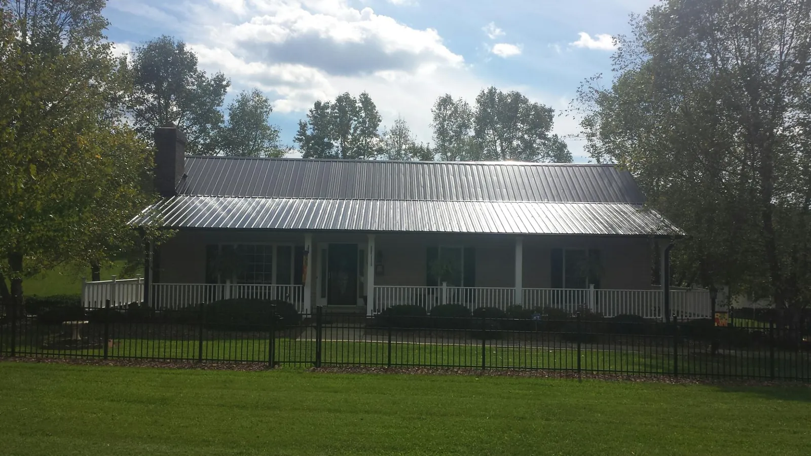 Gray metal roof on a brick ranch with a full width front porch — Gutter Guard Installation work by our crew in Saint Stephen