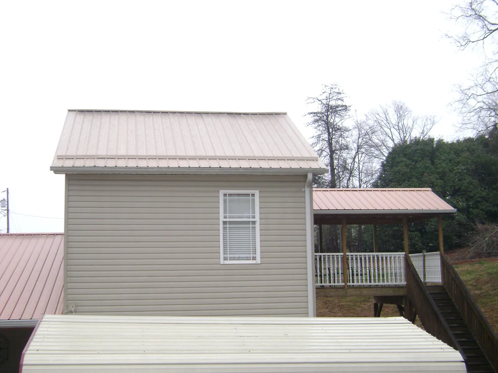 Tan metal roofs on a two story addition and attached porch, from a Roof Replacement job in Saint Stephen